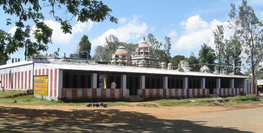 Kollimalai temple with striped walls, domed towers, and surrounding trees under a blue sky.