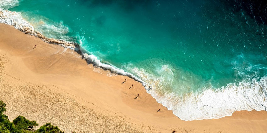 A drone shot capturing the shoreline of a beach, showcasing the contrast between soft sands and clear blue waters.