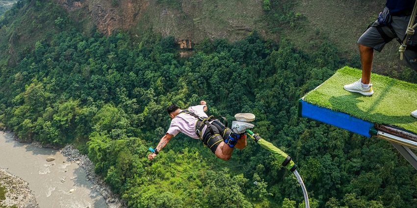 Image  of a man bungee jumping with the view of lush forests down below