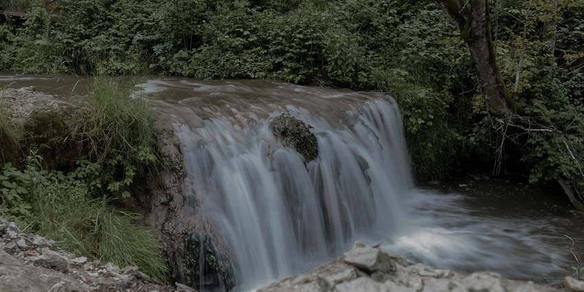 Small waterfall cascading over rocks and many dried leaves fall on the slippery rocks.