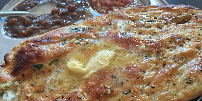 A picture of a delicious kulcha with butter on top, served alongside nihari and salad