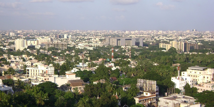 Aerial view of Chennai city with high-rise buildings, greenery, towers, and a church.