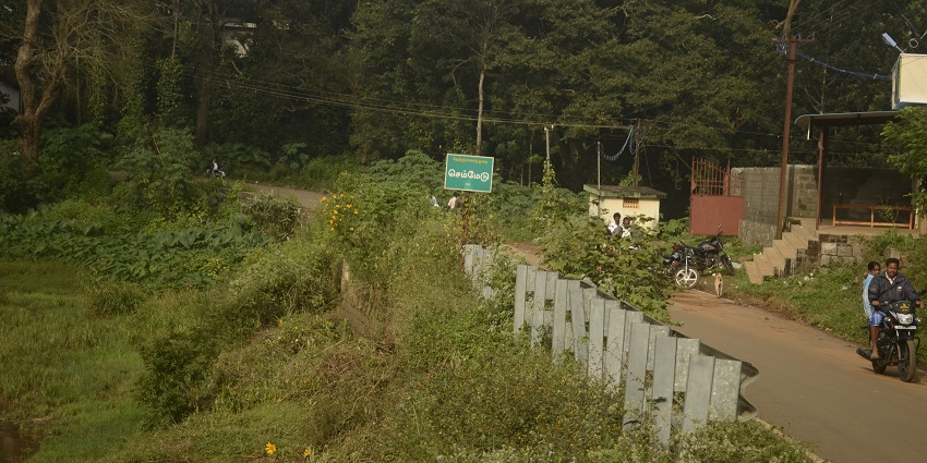 Rural road in Kolli Hills with people and motorcycles, surrounded by greenery and trees.