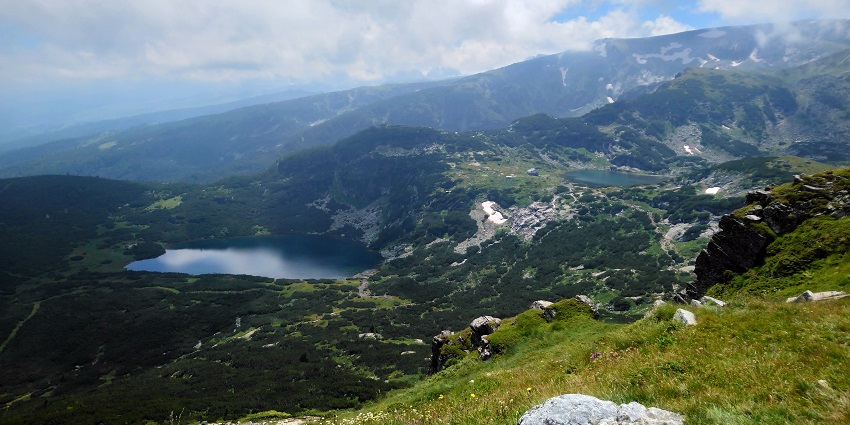 Rila mountain range with small lakes in the middle of the range and surrounded by greenery.