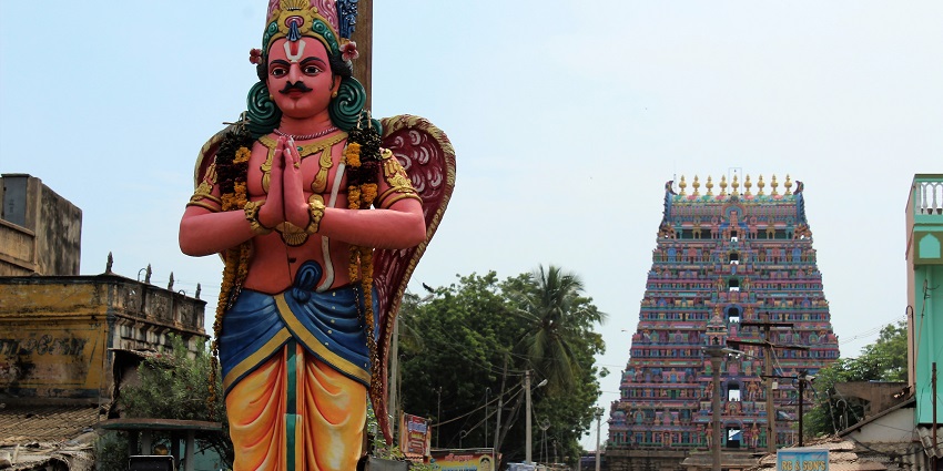 Streets crowded with people and a big statue of the lord at a distance from a temple.
