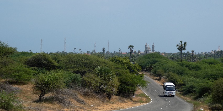 A road surrounded by greenery near Manapad with a single bus travelling through it
