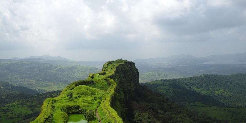 A scenic picture of Lohagad Fort surrounded by lush greenery and cloudy weather.