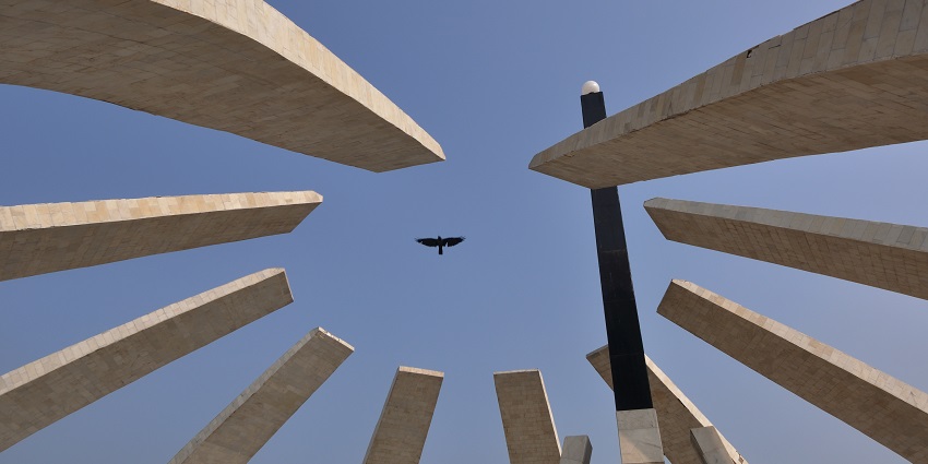 A crow flies above the MGR memorial at Marina Beach in Chennai, India, on a sunny day.