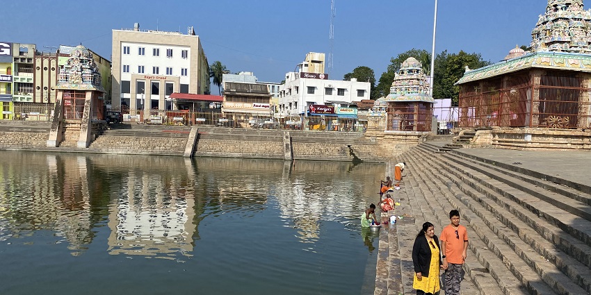 Mahamaham Tank with steps leading down to the water, surrounded by structures and people.