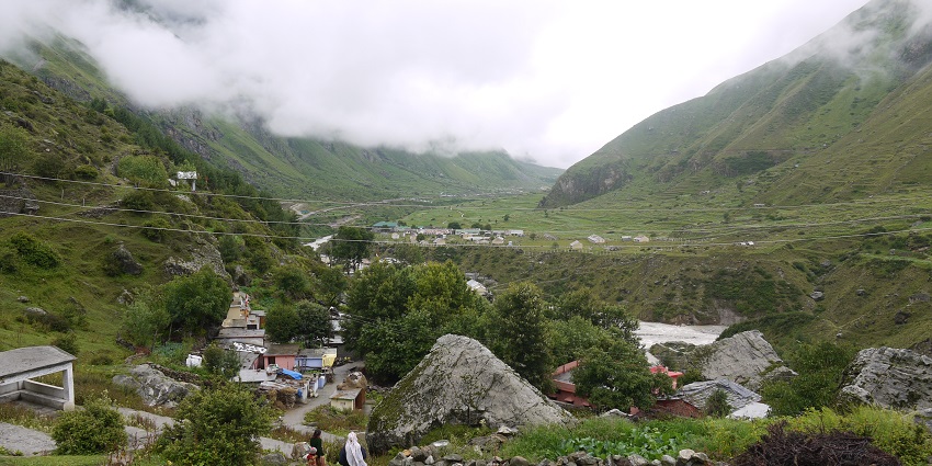 A view of a small village in the mountains, surrounded by green hills under a clear blue sky.