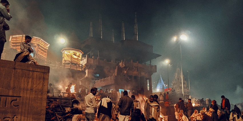 Manikarnika Ghat in Varanasi, with funeral pyres and devotees along the Ganges River.