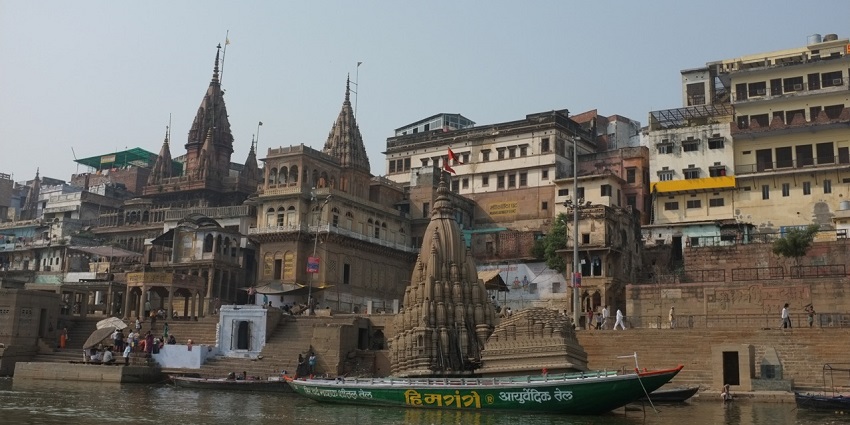A scene of multiple funeral pyres burning at Manikarnika Ghat, Varanasi, India, during the day.