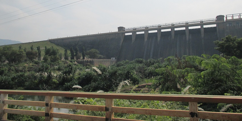 A picture of a huge dam taken from a distance, with lush greenery all around