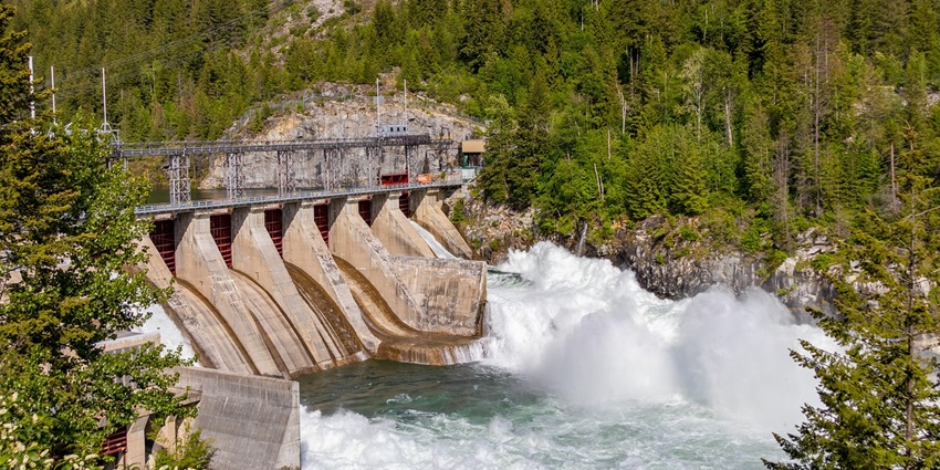 An image of a Maravankandy dam with a lot of water flowing across it, with green trees all around.