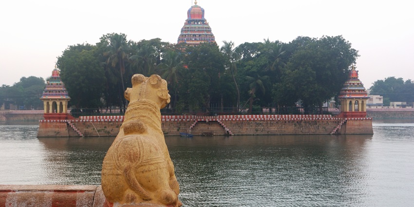 A front view of the Mariamman Teppakulam surrounded by shimmering blue waters.