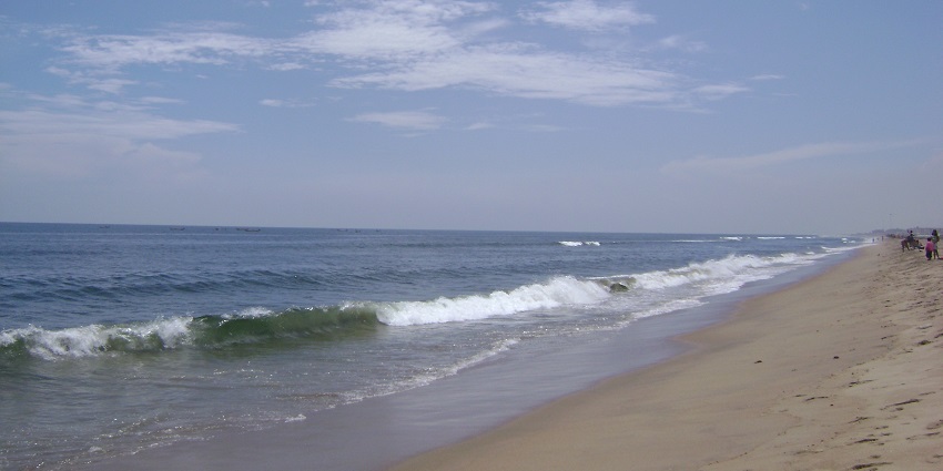 Gentle waves crashing at the shore of Marina Beach with people visible from a distance.