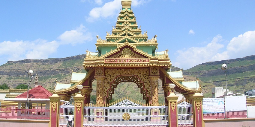 A grand red-and-gold arched gateway with intricate Burmese-style carvings, set against a backdrop of hills