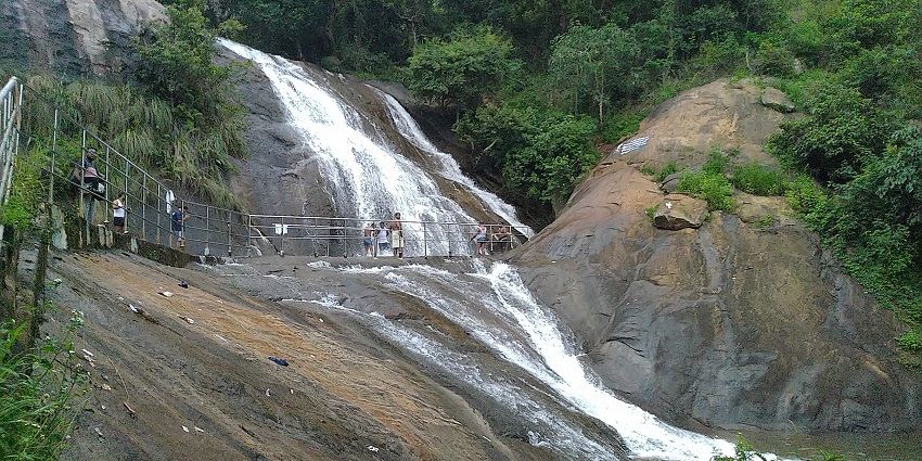 Masila Falls cascading down rocky cliffs, with a bridge and lush greenery surrounding it.