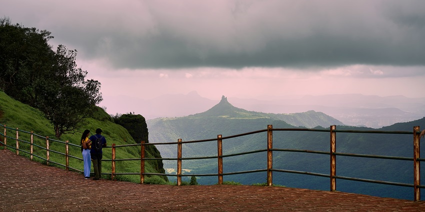 A picture of a couple standing atop a Matheran hillside, enjoying scenic views.