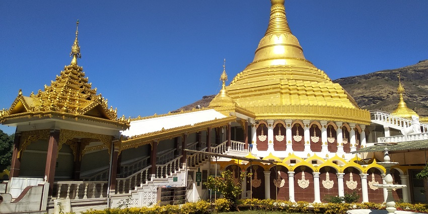 A golden pagoda surrounded by lush greenery at Dhamma Giri, with serene pathways and meditation halls.