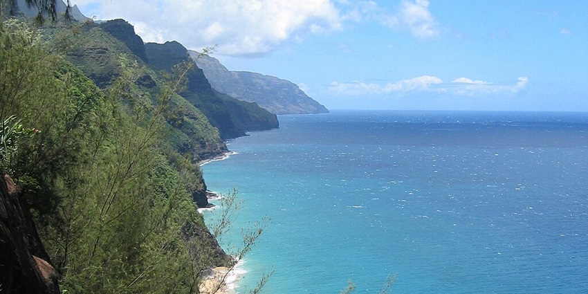 Na Pali Coast State Park with mountains, a shoreline, a clear blue sea and a cloudy sky
