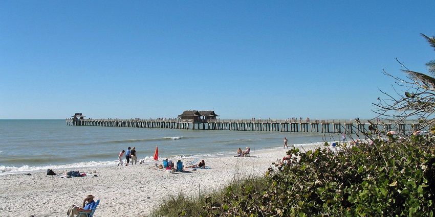 Naples pier with a wooden bridge pathway on it and people enjoying the beachside