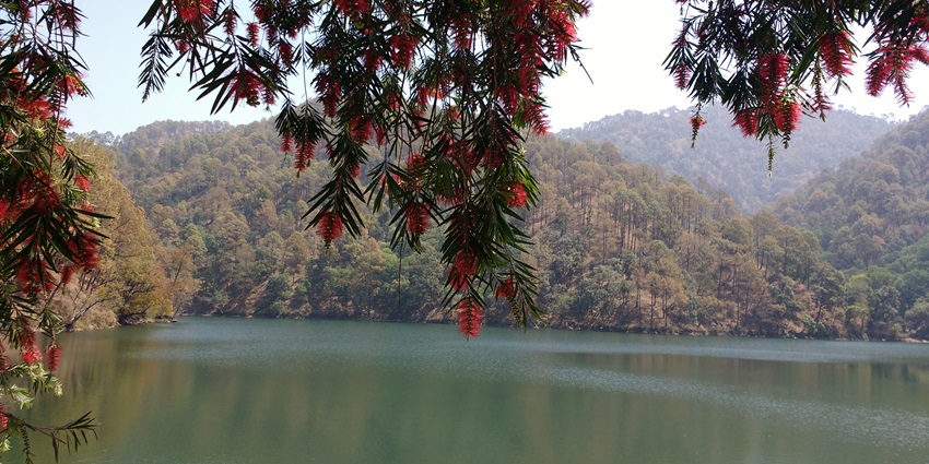 A picture of Naukuchiatal Lake, Uttarakhand that is surrounded by lush green hills.