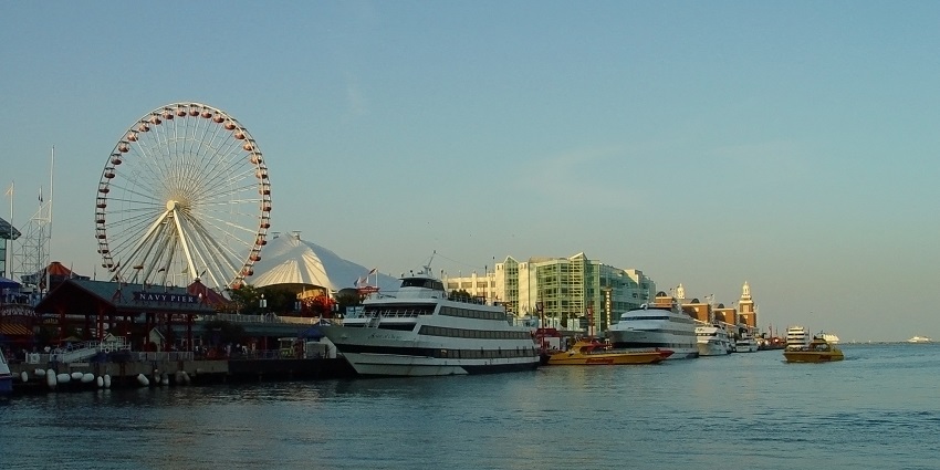 A giant wheel and tall buildings with boats parked in the waters of the Chicago Navy pier