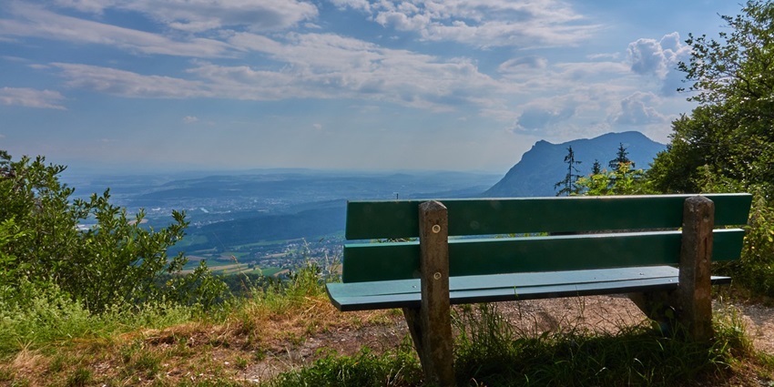 An image of Needle Rock Viewpoint with a green chair on top of a hill looking down at valleys.