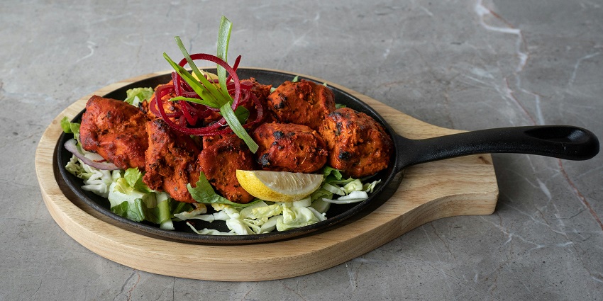 Numerous pieces of tandoori chicken are served with ring onions and lemon wedges