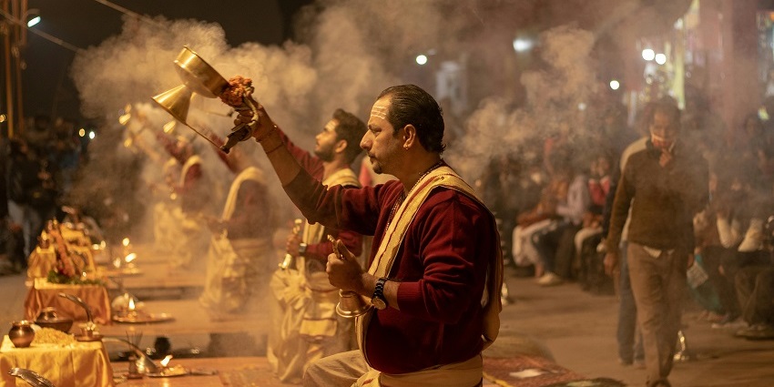 Hindu priests performing pooja with smoke and bells, surrounded by people at night