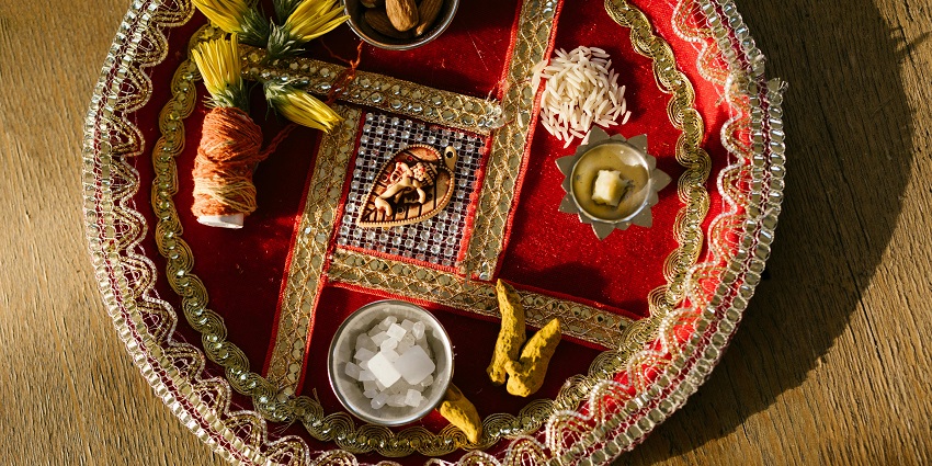 A puja tray with almonds, rice, an alter, turmeric, flowers, red thread and sugar candies