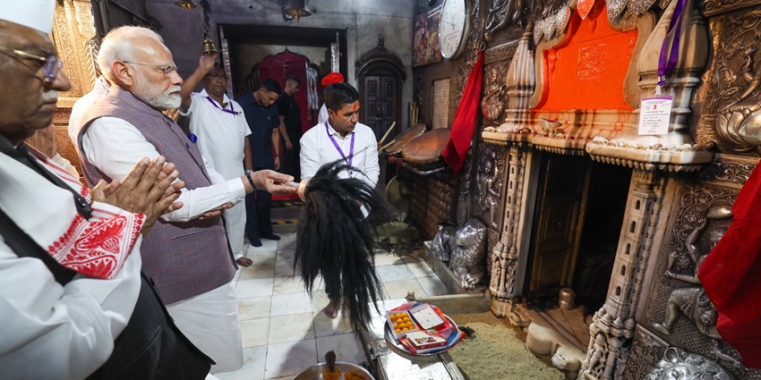 A picture of a devotee offering prayers to a deity’s idol inside a temple with a priest next to him