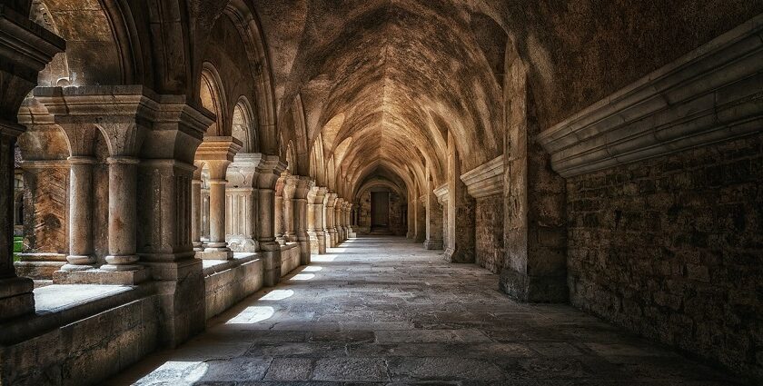 A serene view of a monastery cloister featuring elegant columns and vaulted ceilings, surrounded by lush greenery.