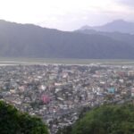 A picture taken from a mountain, showing a city and mountains behind it