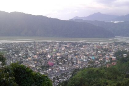 A picture taken from a mountain, showing a city and mountains behind it