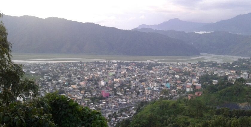 A picture taken from a mountain, showing a city and mountains behind it