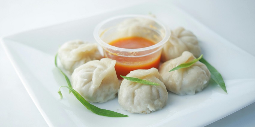 A side view of six pieces of momos placed on a plate while the sauce is in the centre