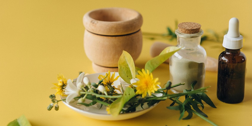 Ayurved lotion bottles placed on a table with coconut, traditional jars and flowers.