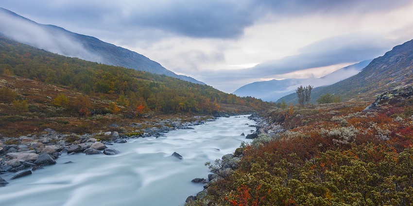 A scenic river valley framed by majestic mountains under a clear blue sky.