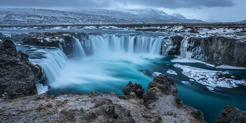 A beautiful view of a waterfall flowing over cliffs, surrounded by dense greenery and mist.
