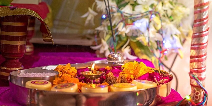 Traditional Hindu pooja thali with lit diya, vibrant flowers, and sacred offerings