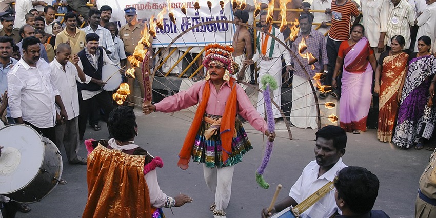 Man dancing with fire and other street performers surrounded by people during a festival