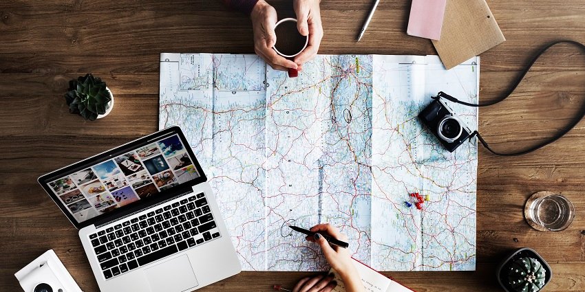 A vacation plan on a wooden table with a map along with other factors to consider.