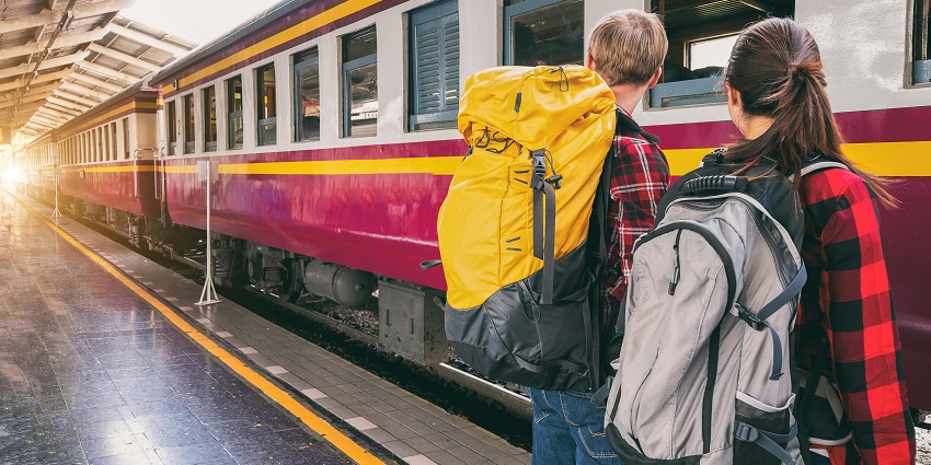 A woman and man waiting to board the train with a train approaching in the background.