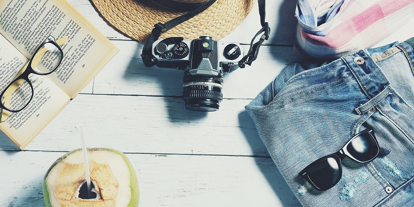 Cloths, a hat, a camera, a book and glasses put on a wooden platform with a coconut.