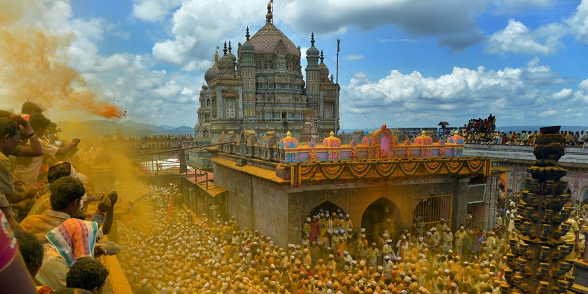 An image of devotees celebrating with turmeric at a huge temple during a vibrant festival.