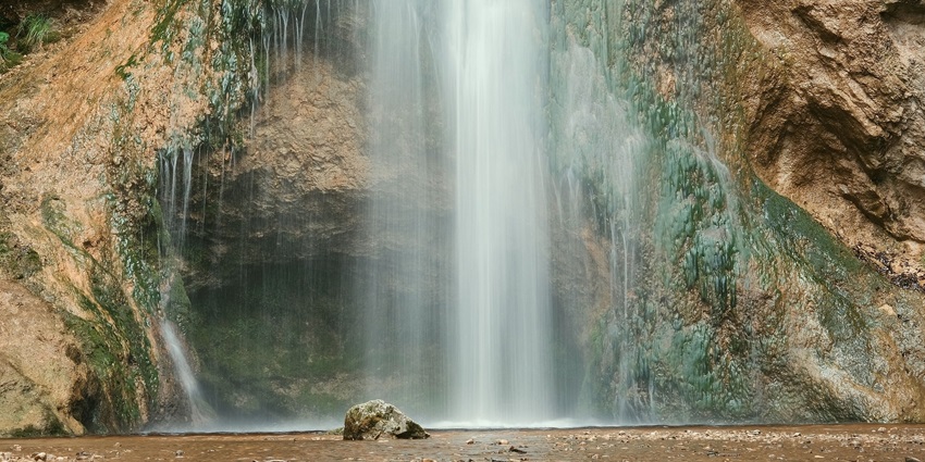 An image of a majestic waterfall cascading over rocks into a serene pool, surrounded by lush nature.