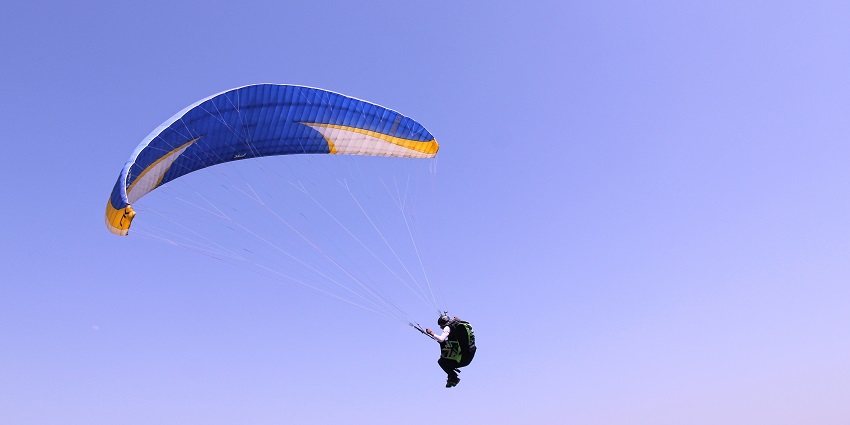 Image of a man soaring through the sky, paragliding with the blue sky in the background