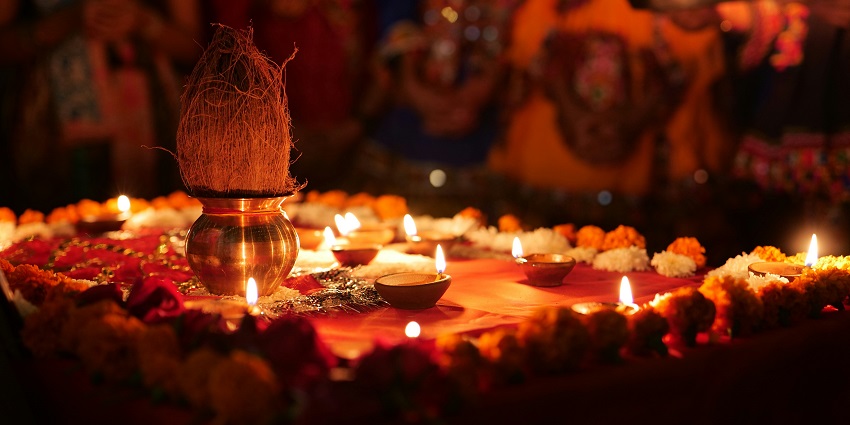 A burning clay diya placed with other diyas on a floor surrounded by broken flower petals.